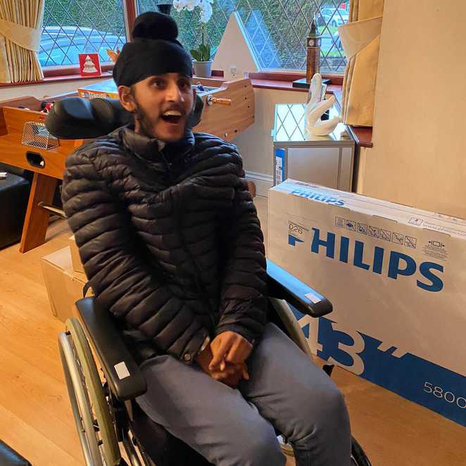 Sunil sitting in his wheelchair with a huge smile, while surrounded by his Christmas presents.
