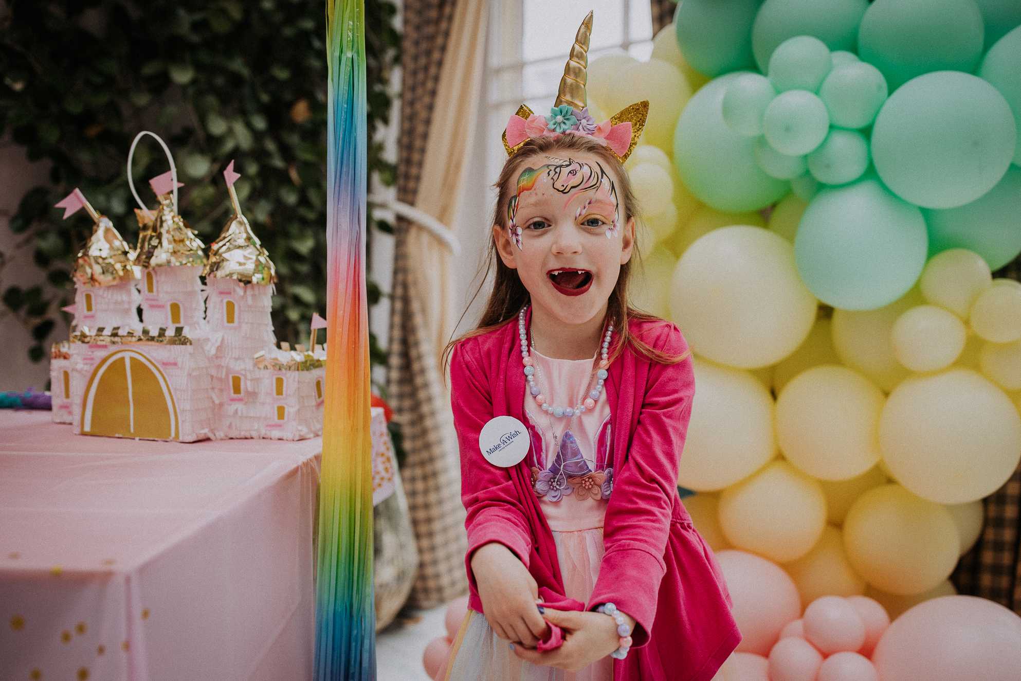 Lacey with unicorn facepaint and horn smiles at the camera with balloons alongside her
