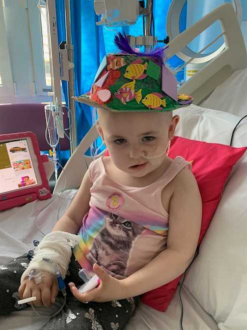 Ryleigh wearing a colourful, hand-decorated hat while receiving treatment in hospital.