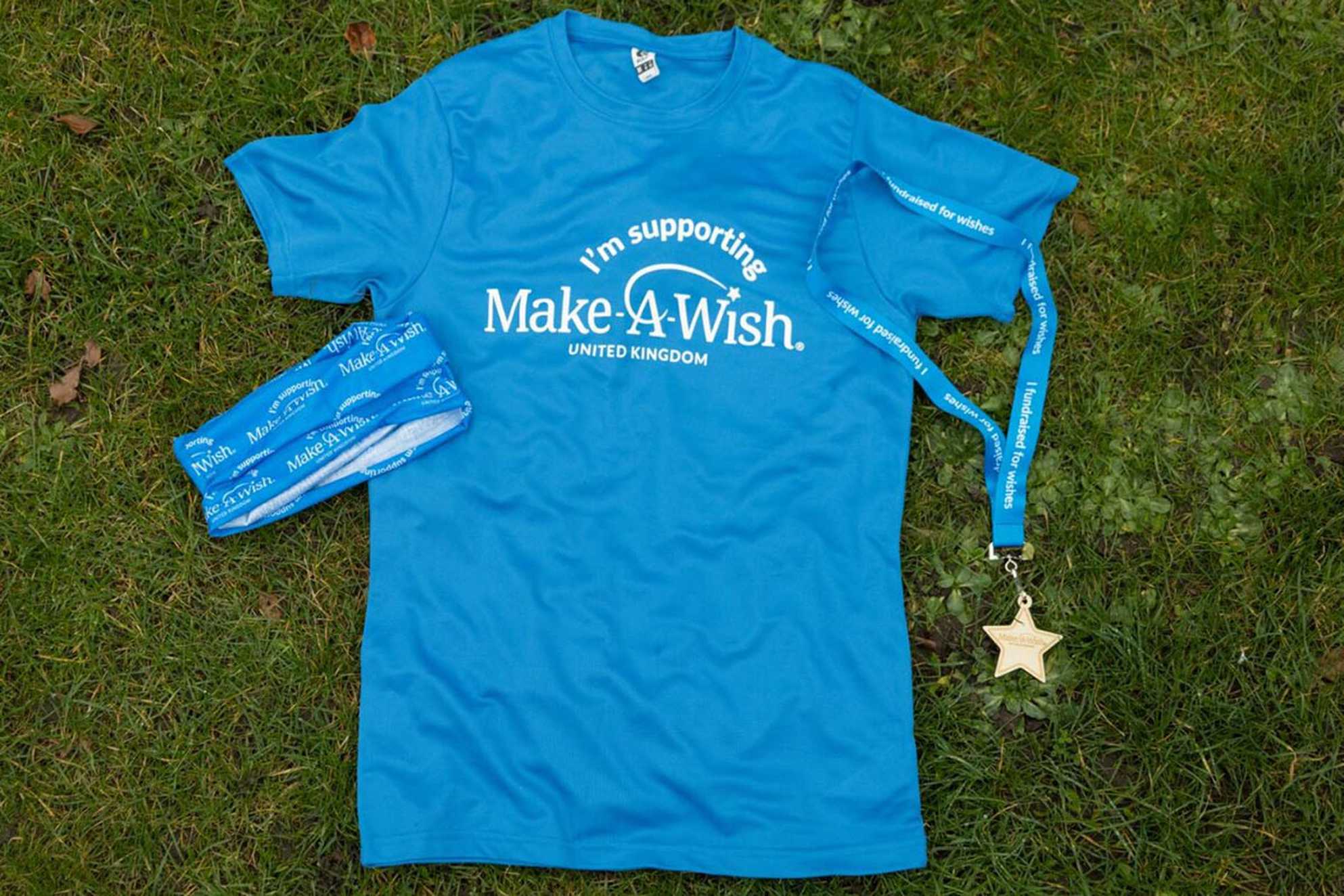 A Make-A-Wish UK t-shirt, buff and medal laid out flat on a grassed area.
