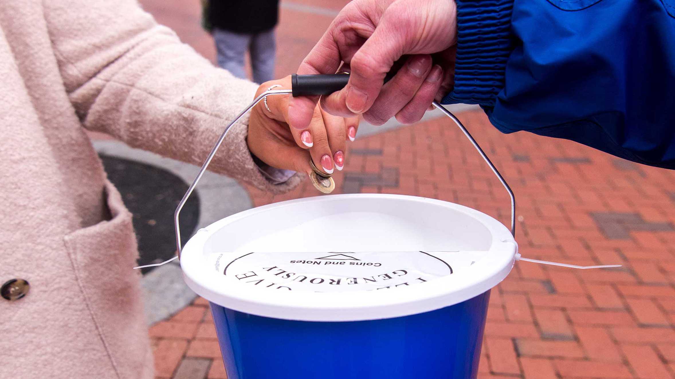 Someone putting money into a donation bucket.