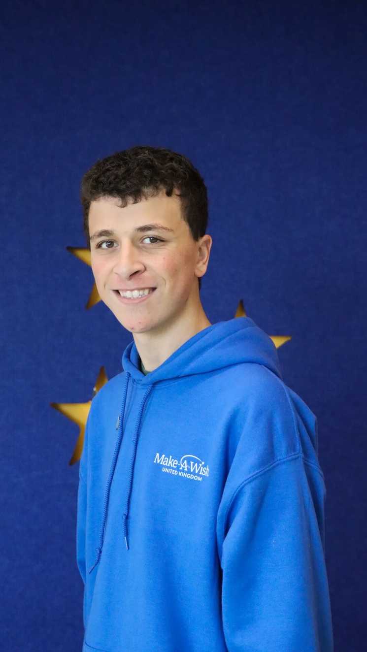 STARboard member Theo is looking at the camera, he is wearing a blue Make-A-Wish jumper.
