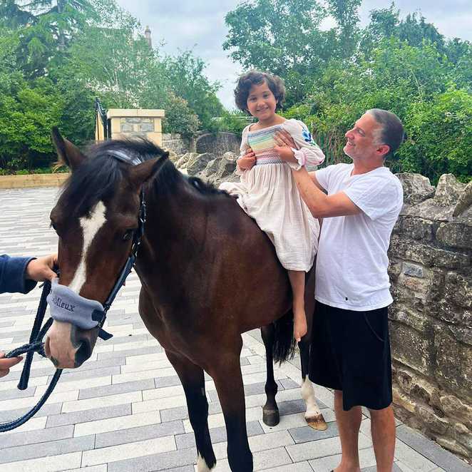 Lila's dad holds her as she sits on a horse during her wish.