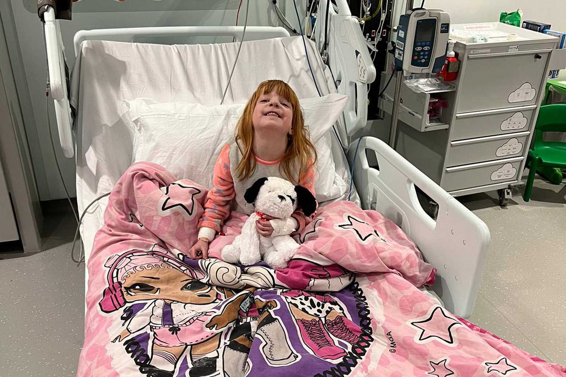 Charlotte smiling bravely in her hospital bed, complete with bright pink covers.