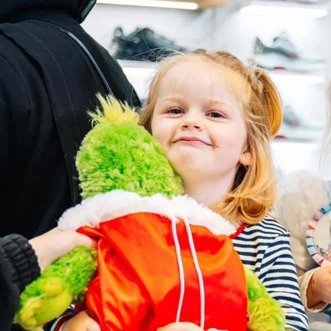 Demi smiles as she hugs her green The Grinch soft toy, whilst sat in a shoe shop.