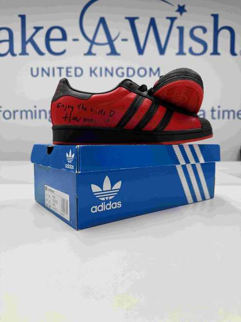 A pair of red and black Miles Morales Adidas trainers on top of their box.  The trainers have been signed byHerman Hulst.