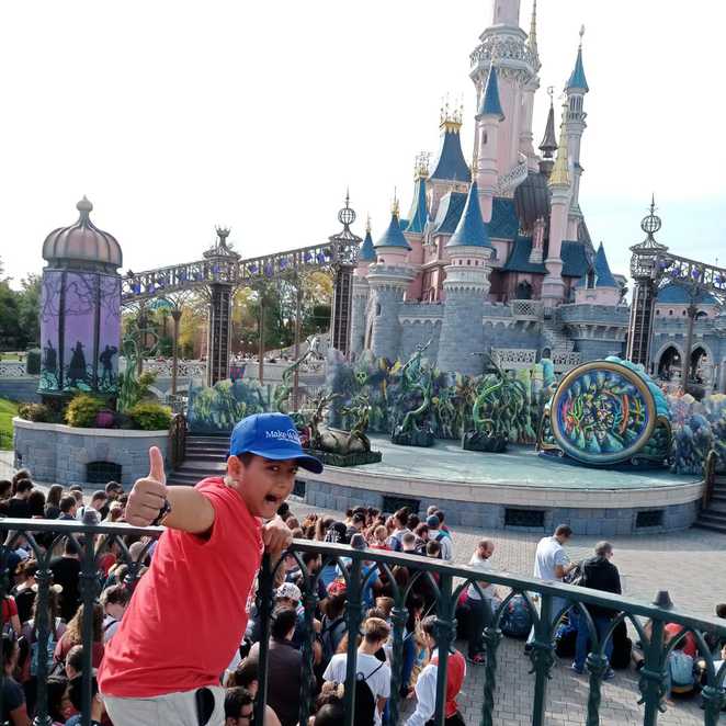 A smiling Abhi giving a thumbs up in front of a castle at Disneyland Paris.