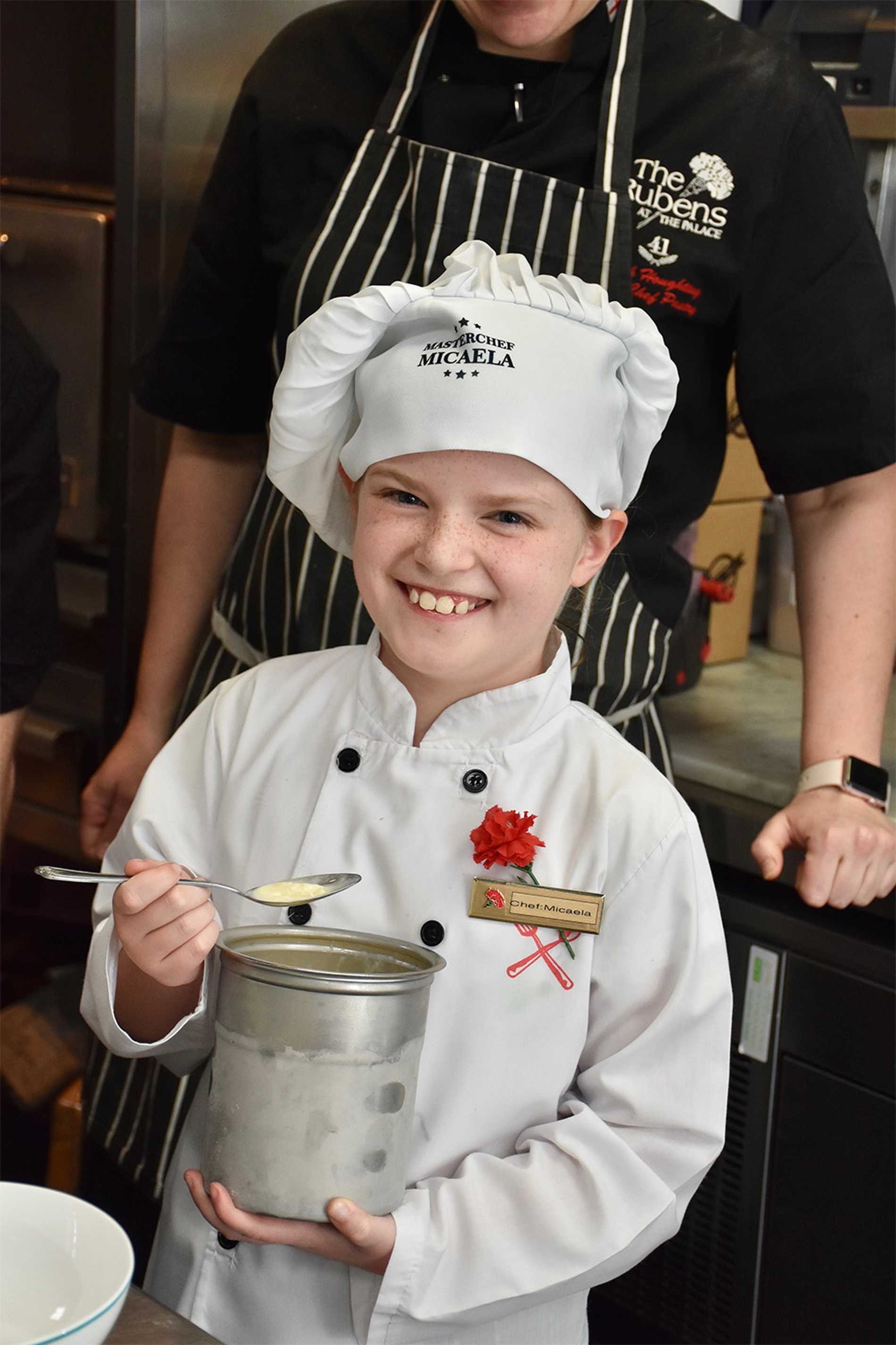 Micaela with a big smile, holding a metal mixing jug with a member of the kitchen team standing behind her.