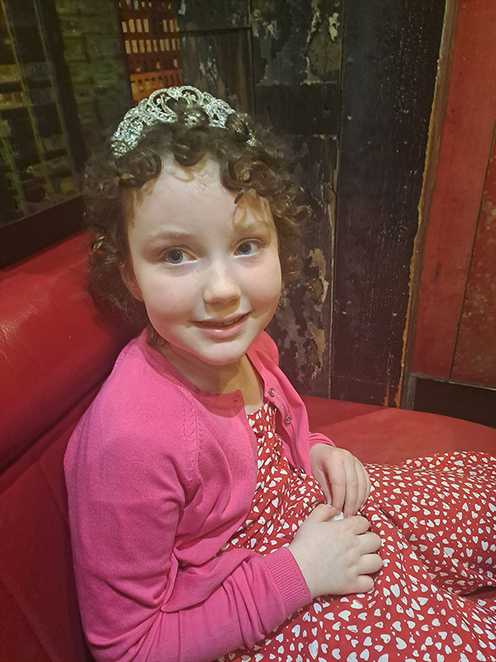 Penelope sits at a restaurant table smiling while wearing a tiara
