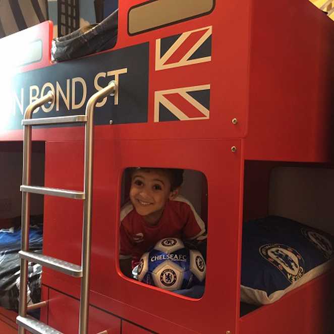 Wish Child Mohommad sitting in his new London bus bed, smiling at the camera.