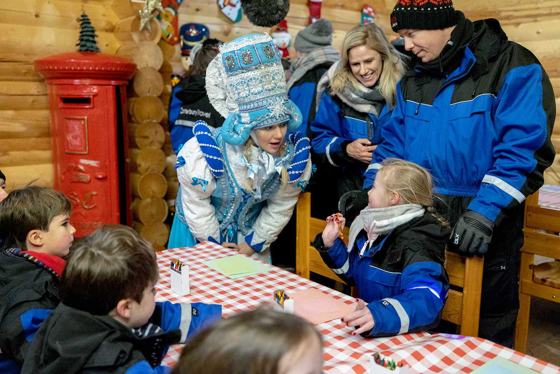 Alice sat at a table with other wish children, chatting to one of Santa's helpers as she writes a letter to Santa.