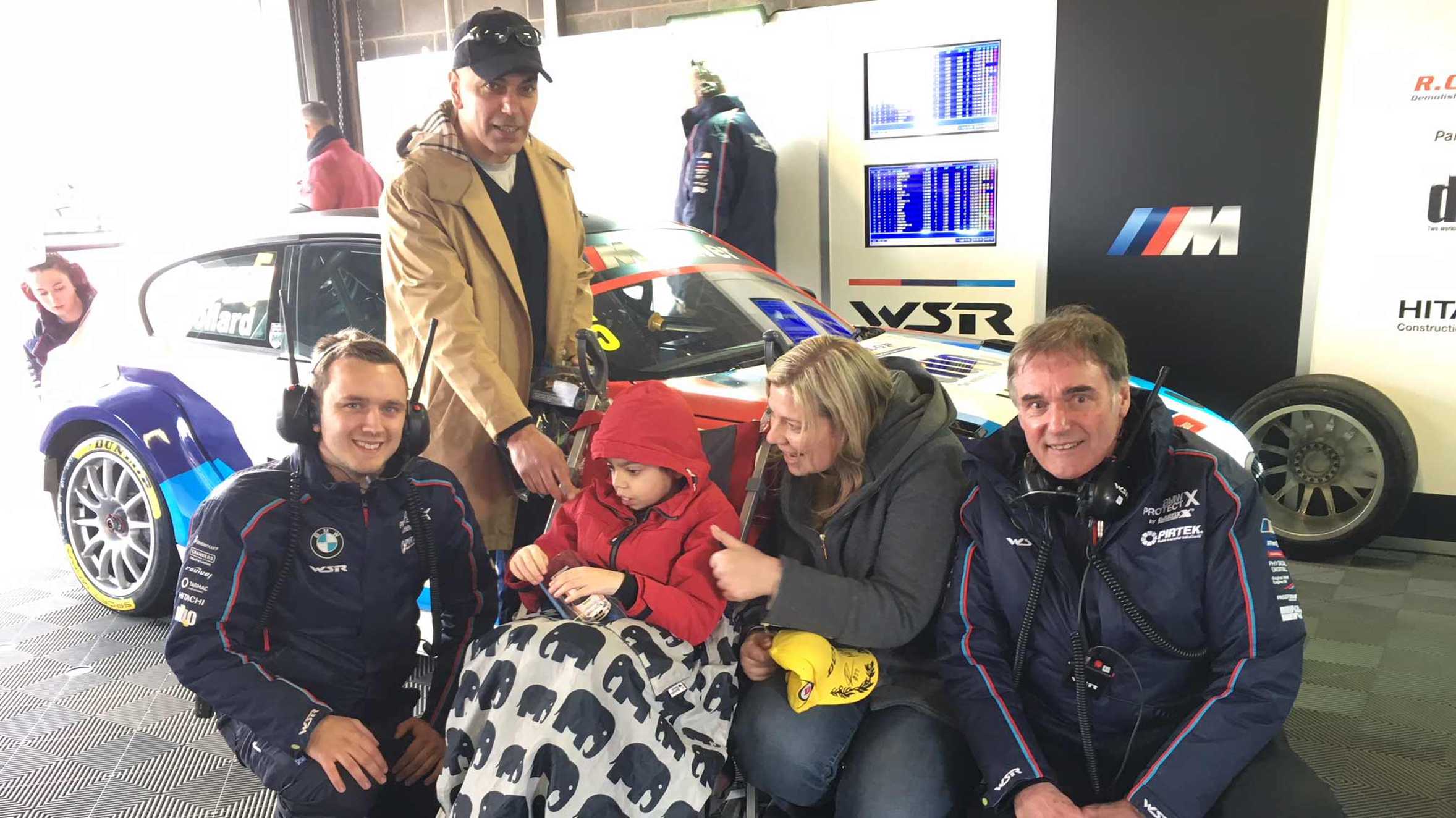 Zaid and family standing in front of a racing car with driver, Matt Neal.