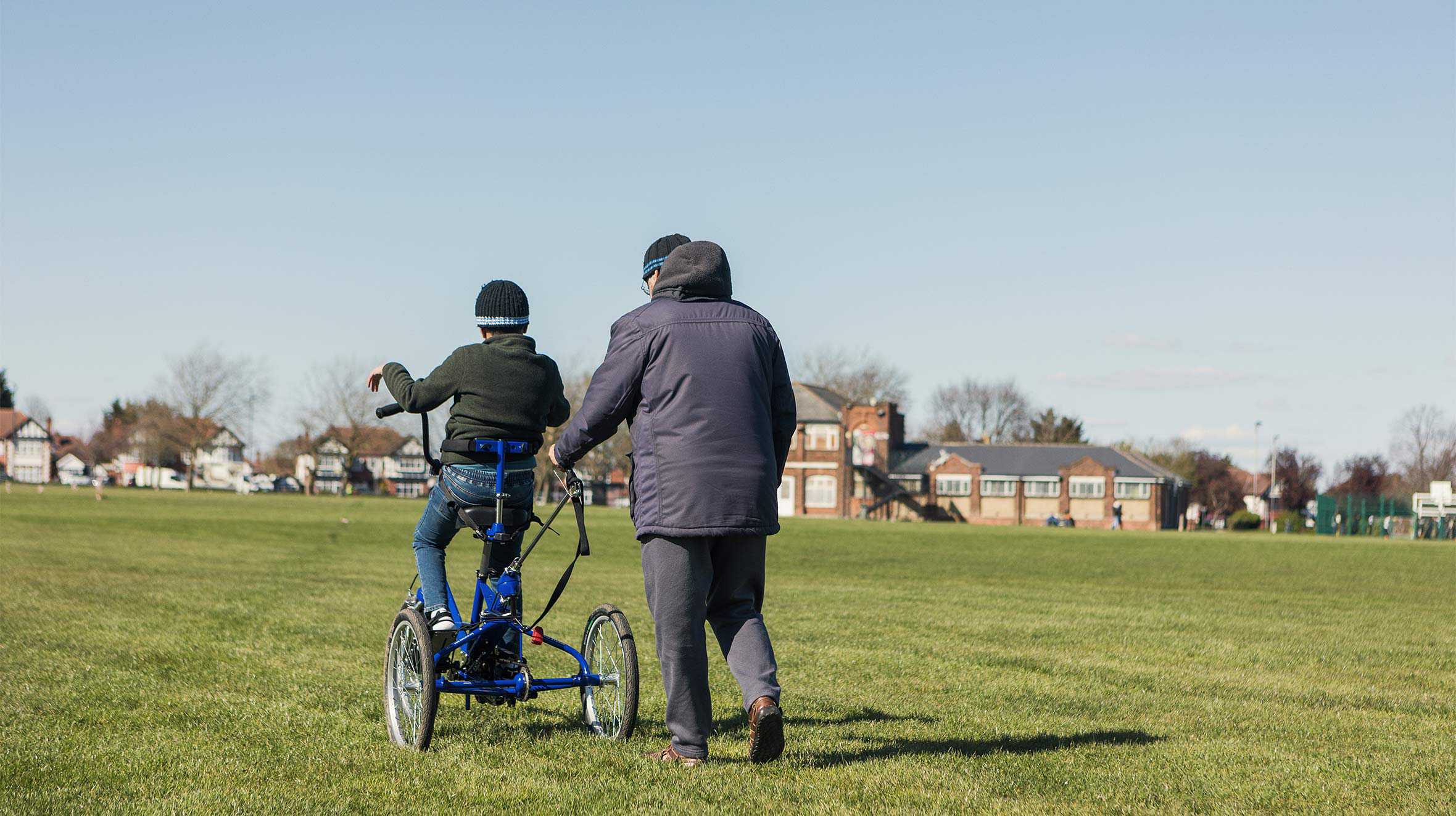 Aaryan cycling away from shot in his local park, as dad, Raj walks behind.