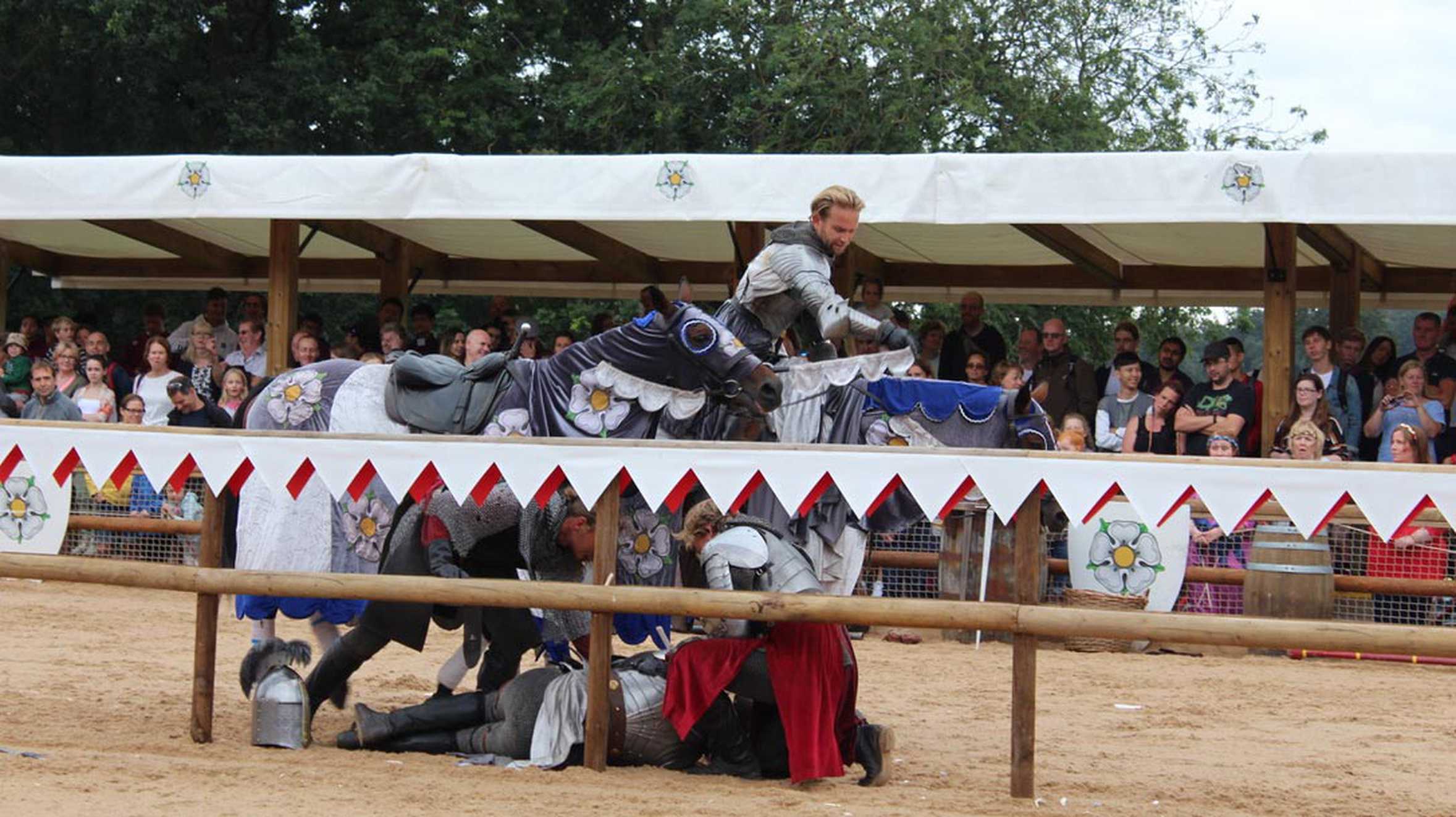 Crowds watch on as a knight recovers after being knocked of his horse during a joust.