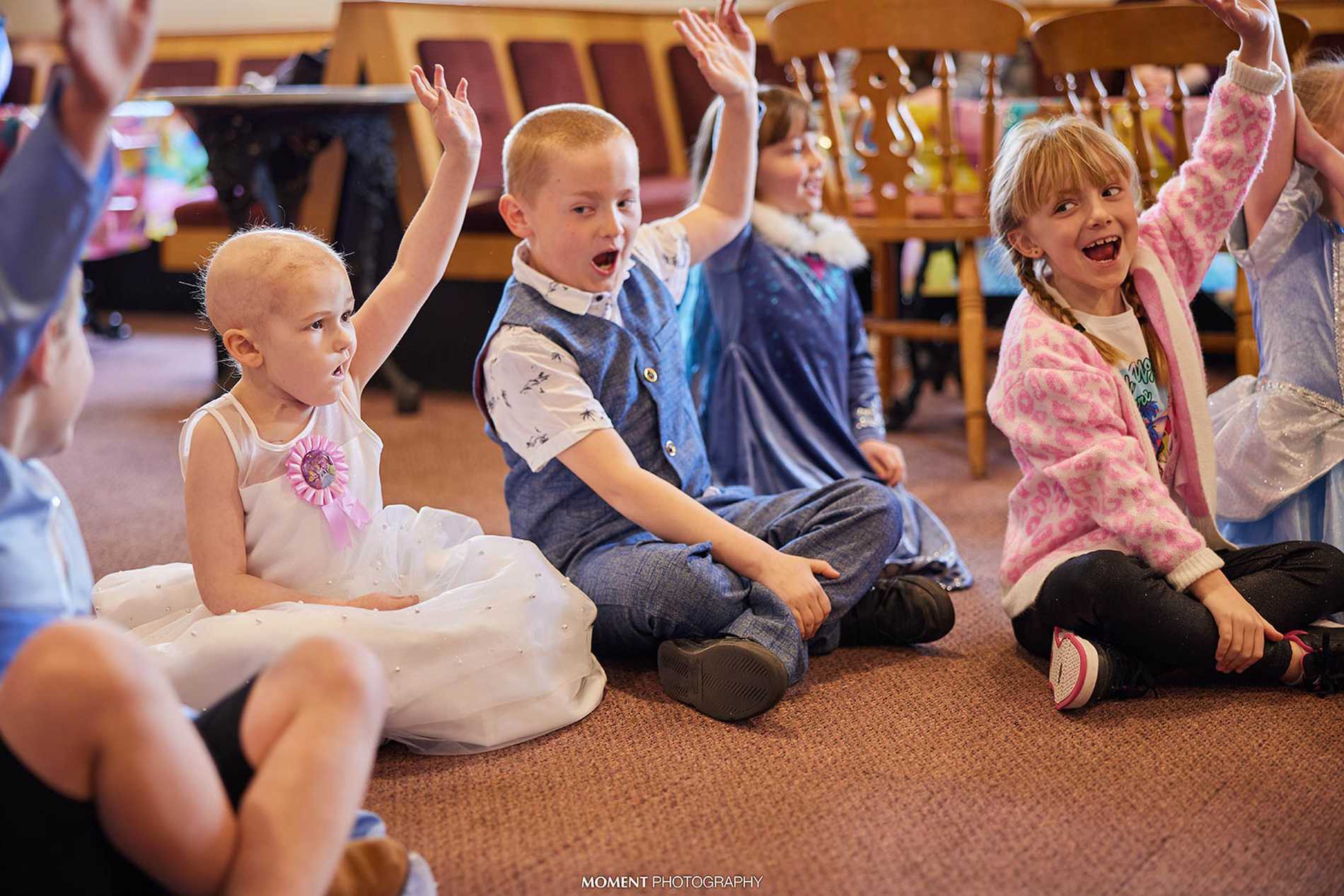 Ryleigh and her friends sitting on the floor with their hands up as they interact with the entertainer.