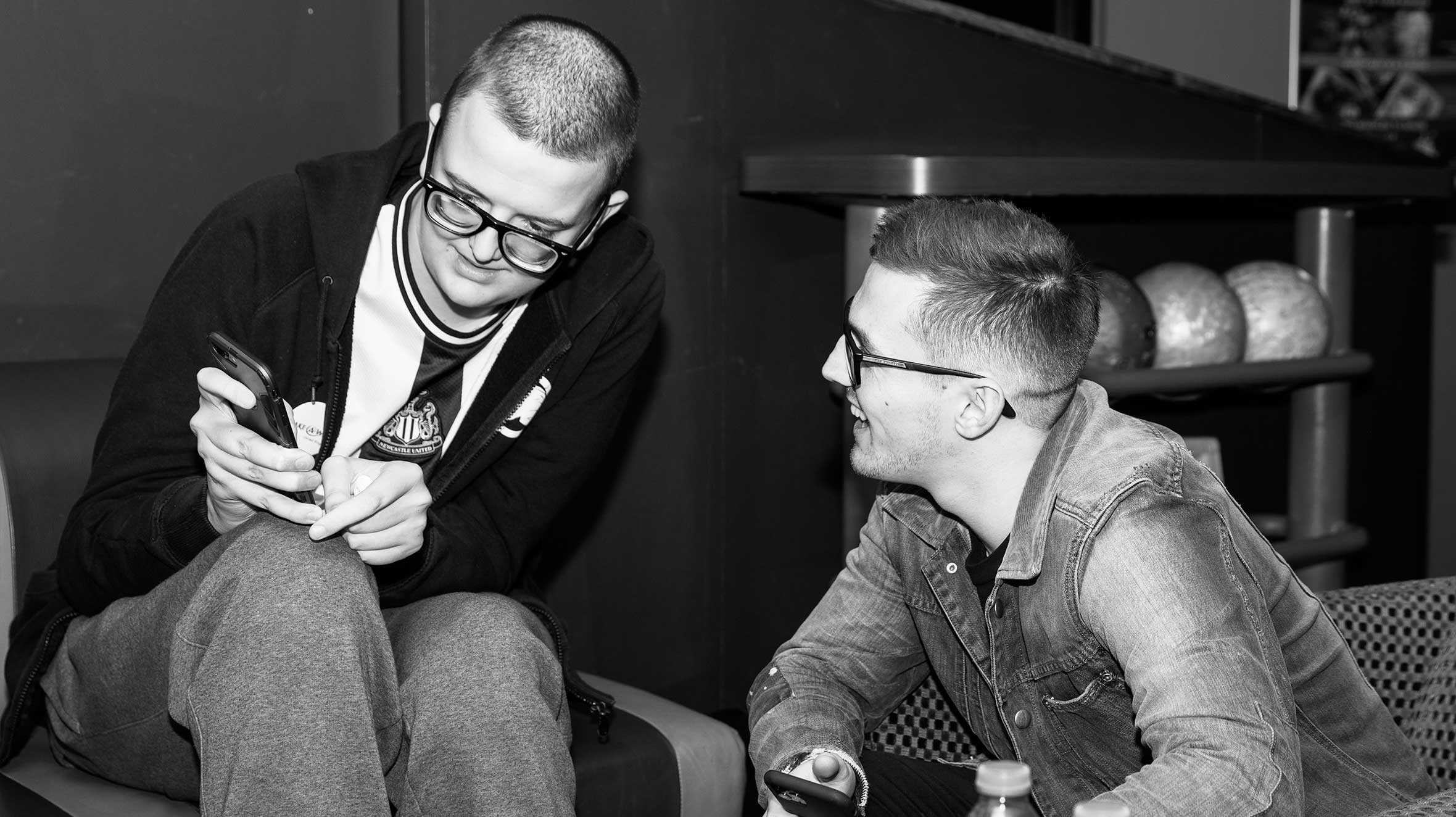 A black and white image of Christopher showing Tom Cassell something on his phone.