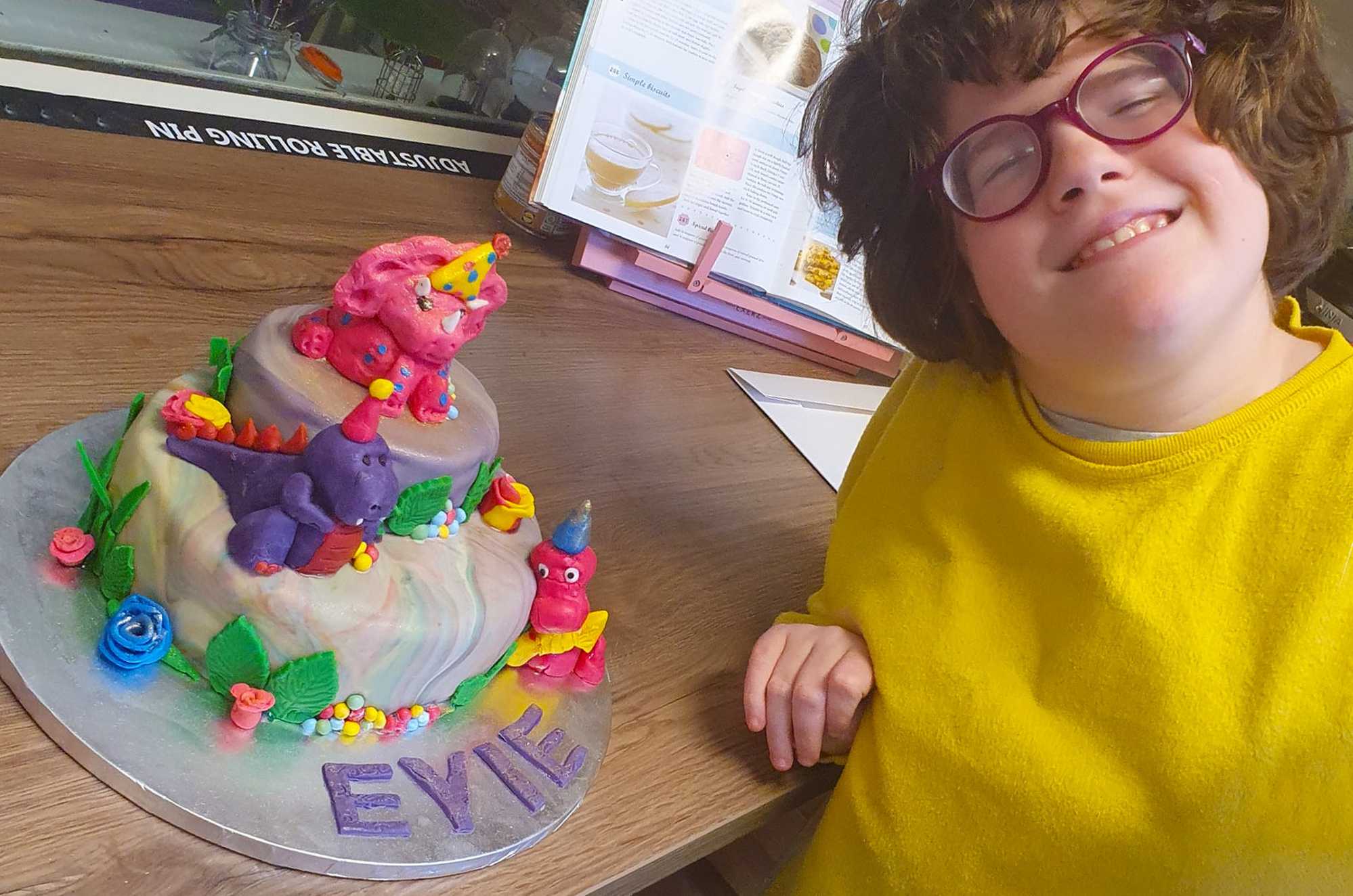A smiling Dakota, proudly showing off a dinosaur-themed cake she's made.