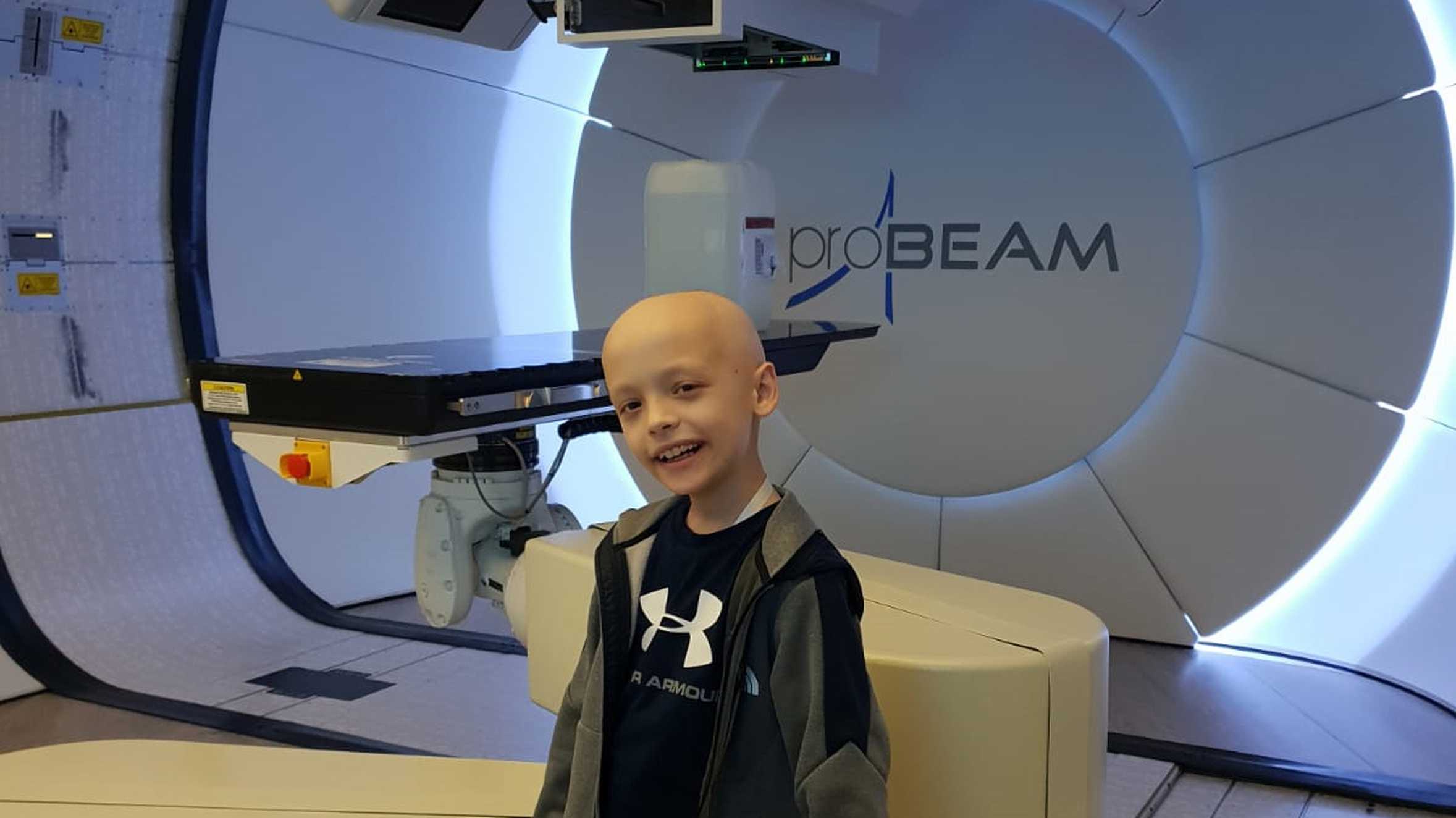 McKenzie posing in front of a large proton therapy machine.