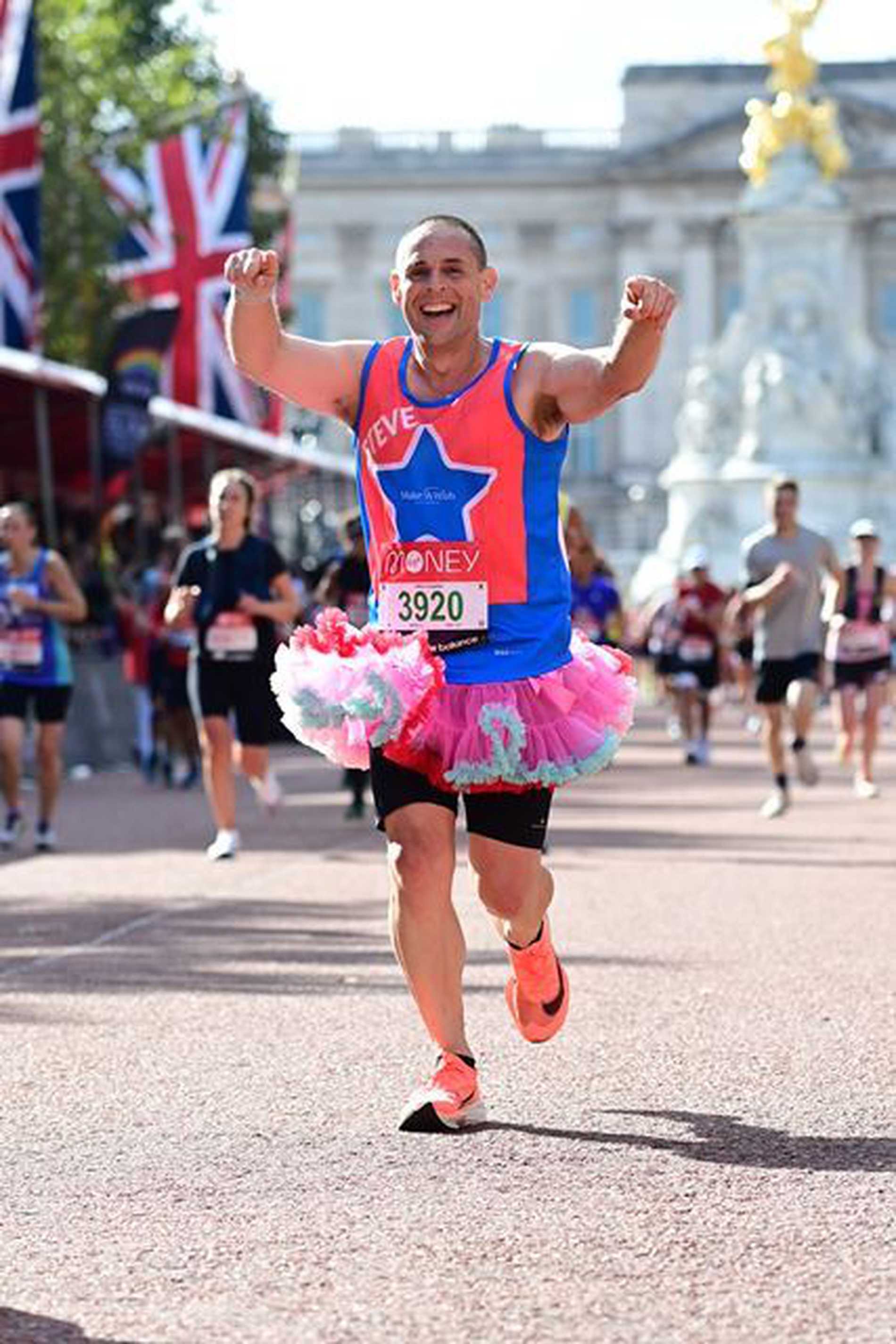 A smiling #WishHero running down the Mall wearing a pink tutu, with Buckingham Palace in the background.