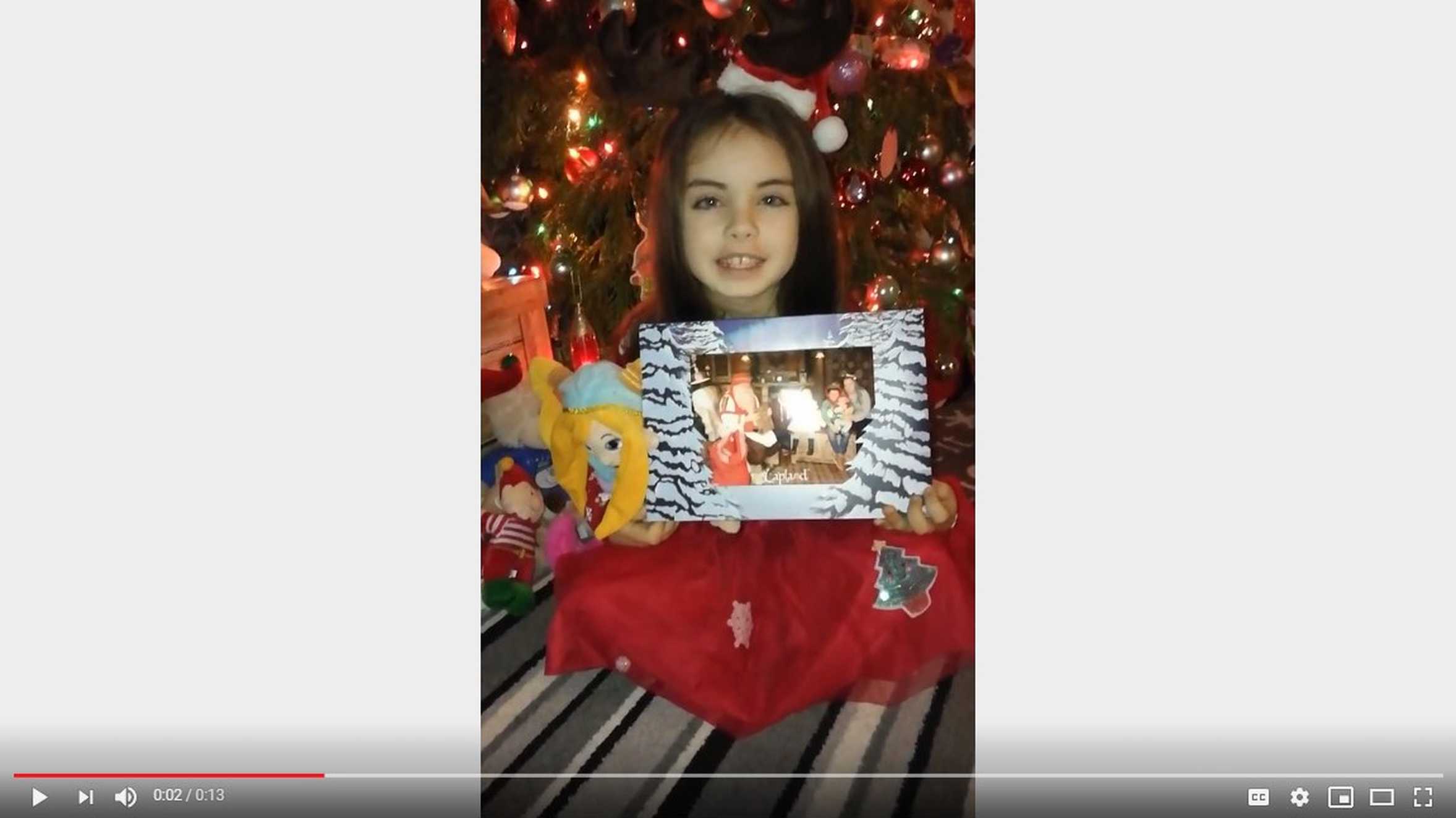 Ella sitting in front of a Christmas tree showing her picture of her meeting Father Christmas