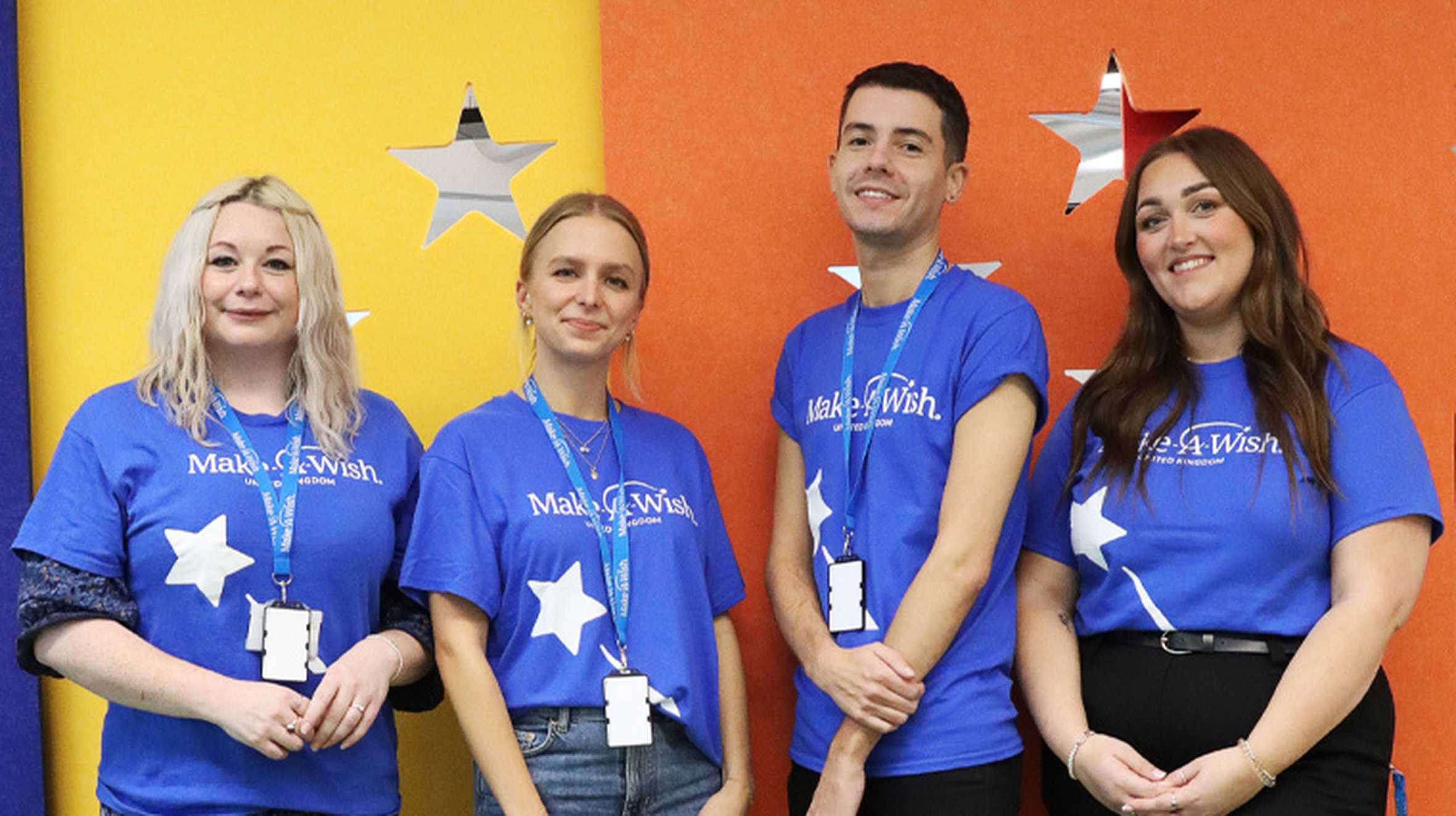 The Make-A-Wish Community Fundraising Team standing in front of a colourful background in Make-A-Wish UK's Reading hub.