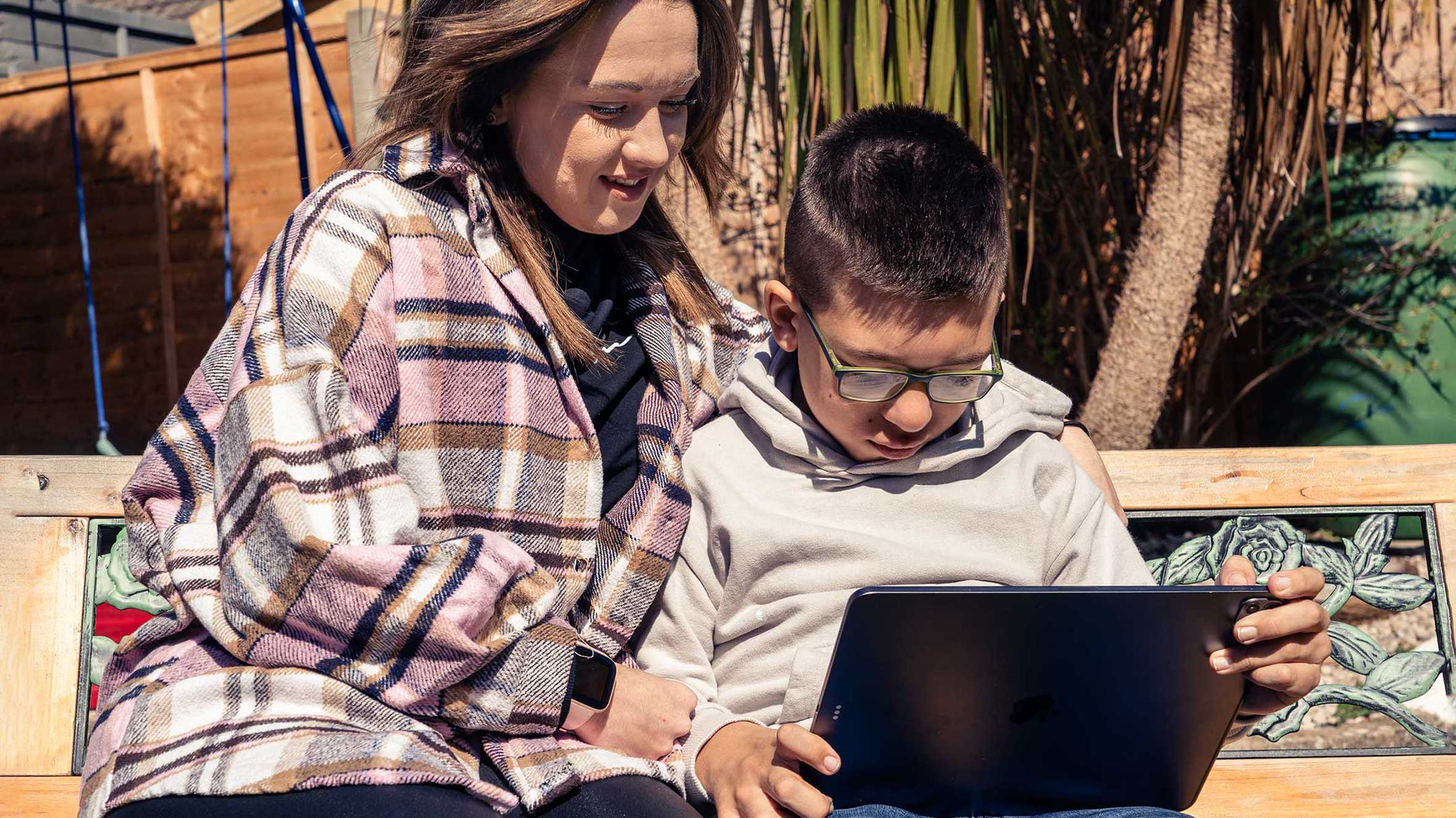 Harvie's mum, Sophia with her arm around him while he plays on his new iPad Pro in the garden.