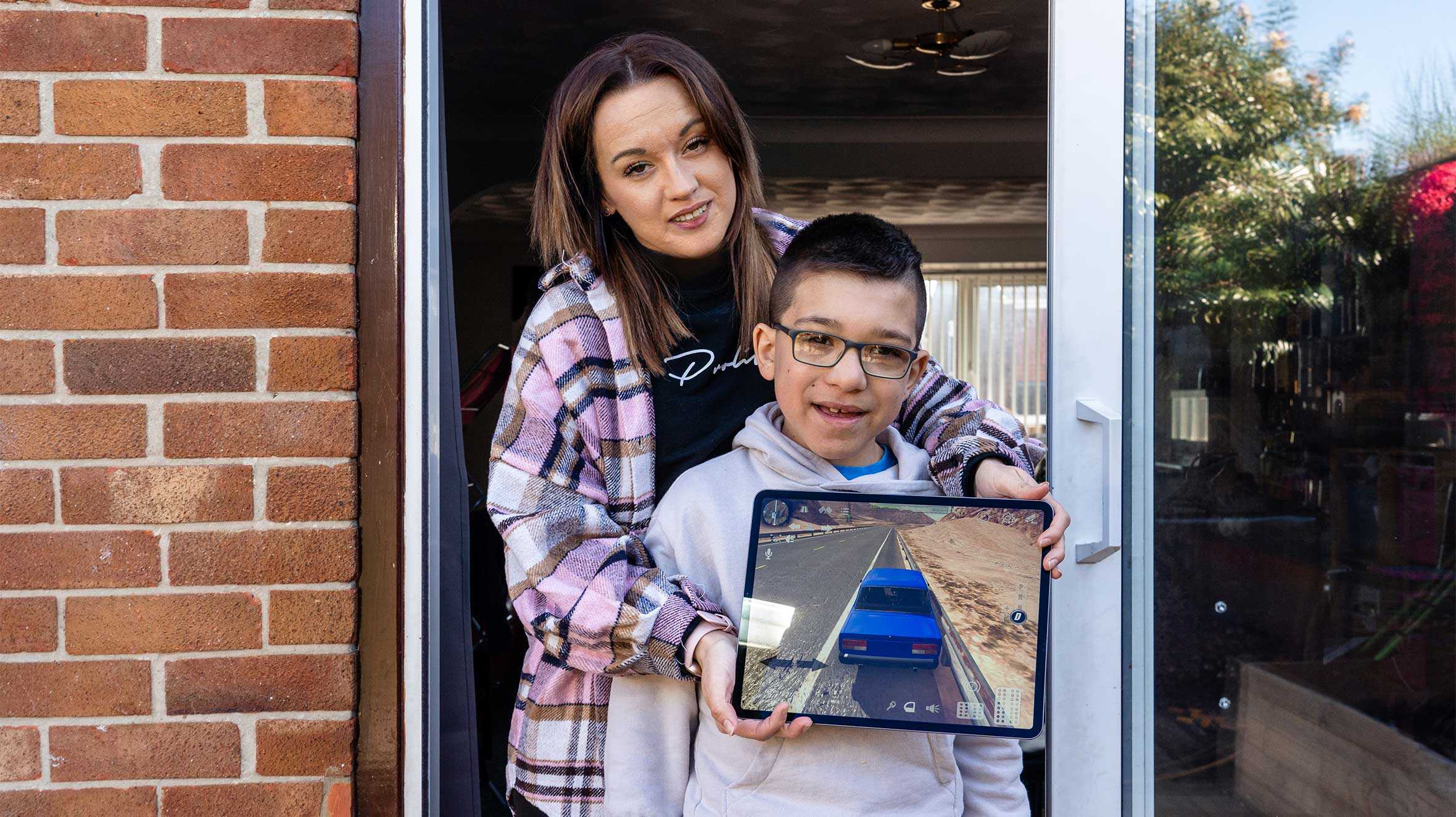 Harvie standing in the doorway with his mum, holding up his new iPad.
