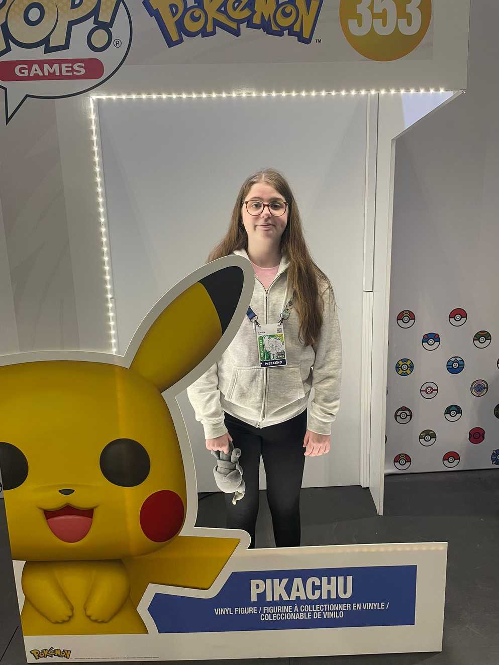 Amelia is wearing a grey zip hoodie and dark wash skinny jeans. She is stood smiling for the camera inside a human-size toy figurine box. On the cover of the box is a large yellow Pokémon character called Pikachu.