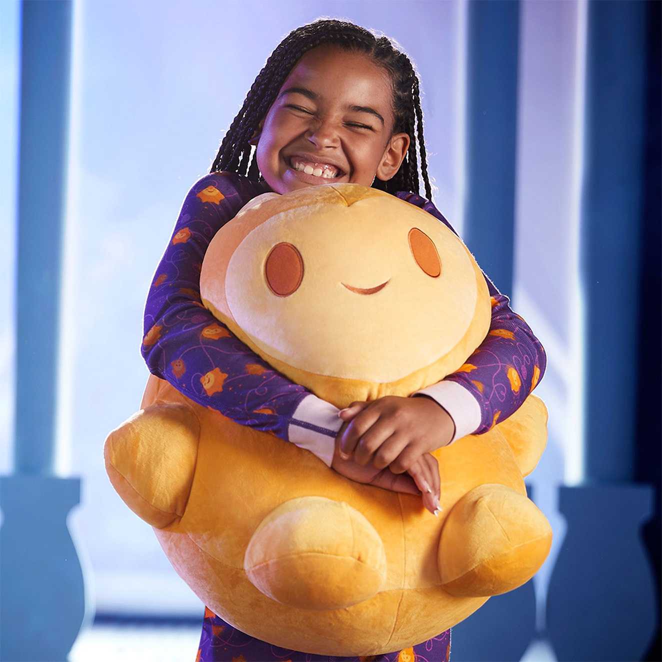 A smiling child cuddling a large yellow Disney plush toy from the Shop Disney Wish Collection.