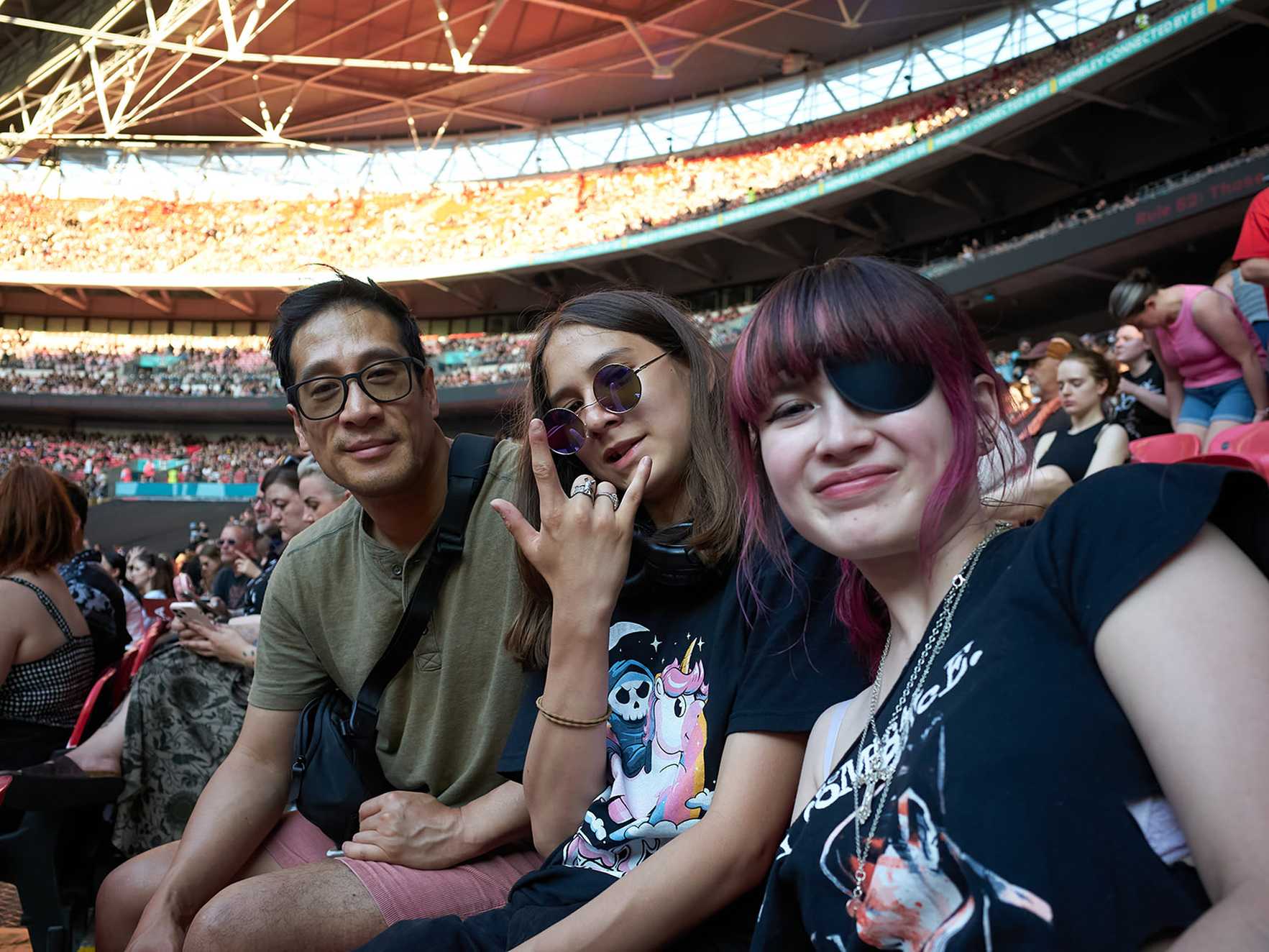 Phoebe, her dad and brother smile in the seats at Wembley Stadium on a summer evening