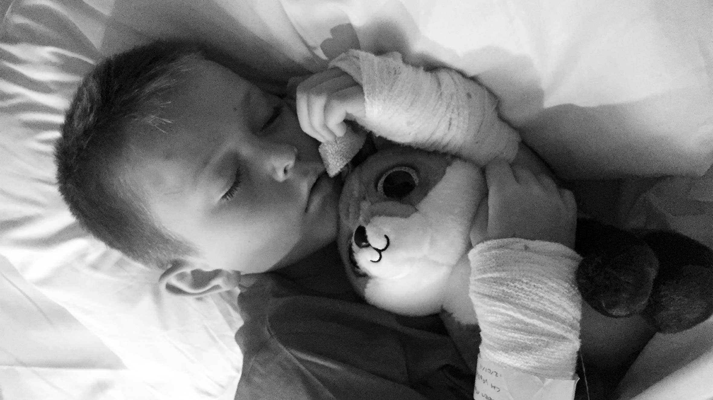 Black and white image of Caden sleeping in hospital while holding a cuddly toy