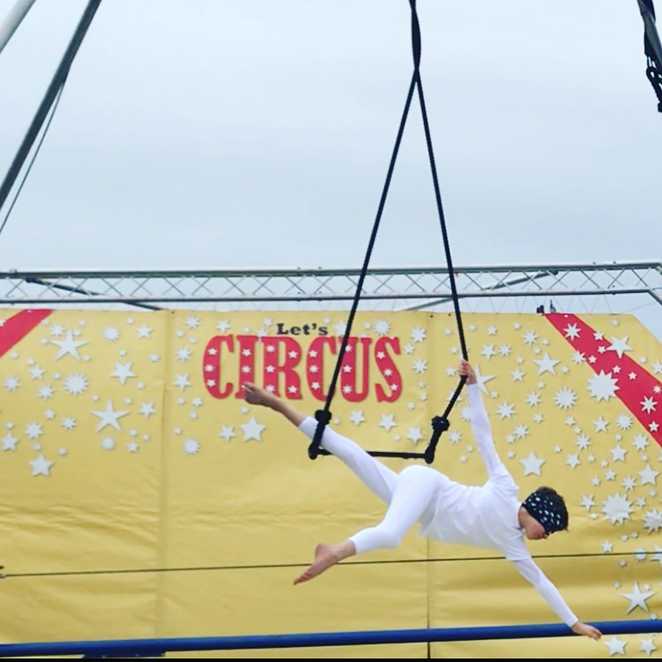 Wish child Sam in a white outfit, performing on the trapeze while blindfolded.
