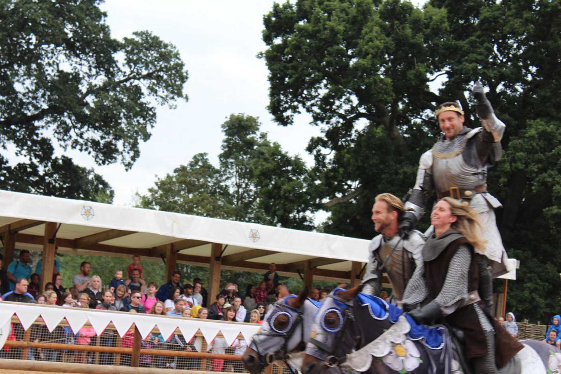 A knight standing while straddling two horses that are being ridden by two of his colleagues.