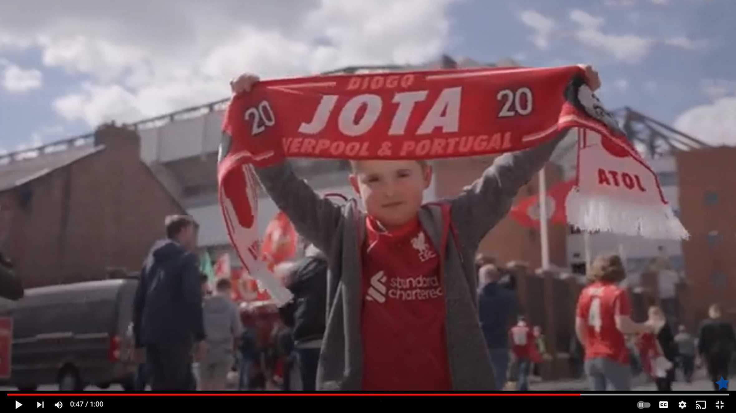 Archie holding up a Liverpool FC scarf outside Anfield Stadium.