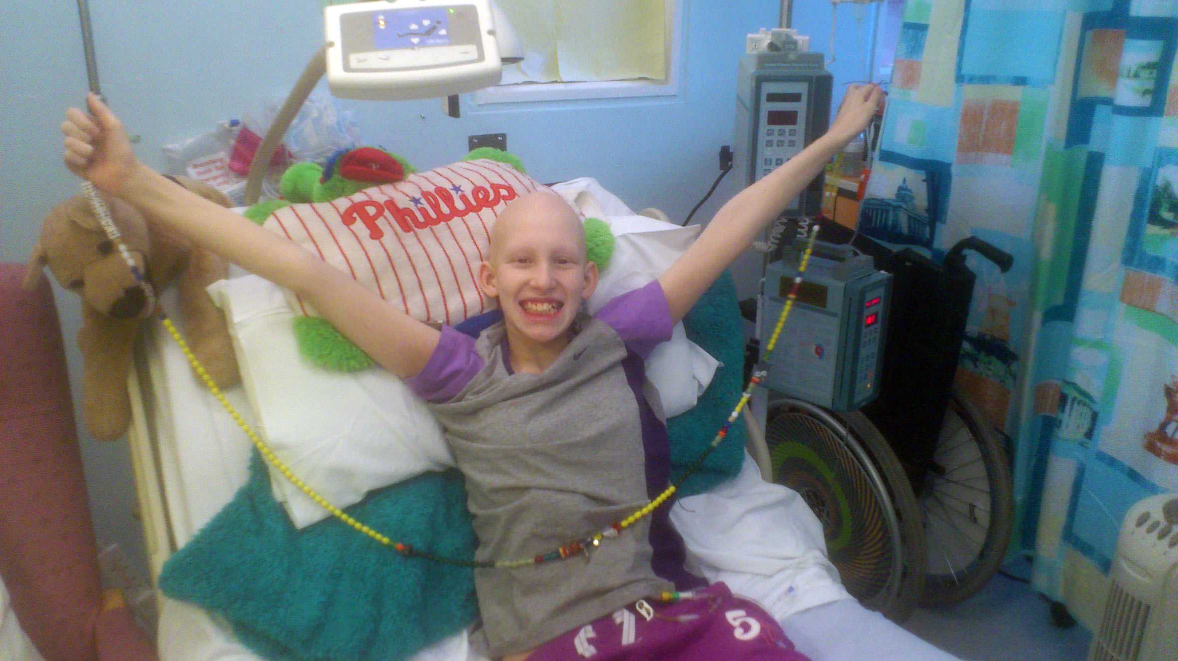 Hannah bravely smiling and holding her arms in the air, while receiving treatment in hospital.