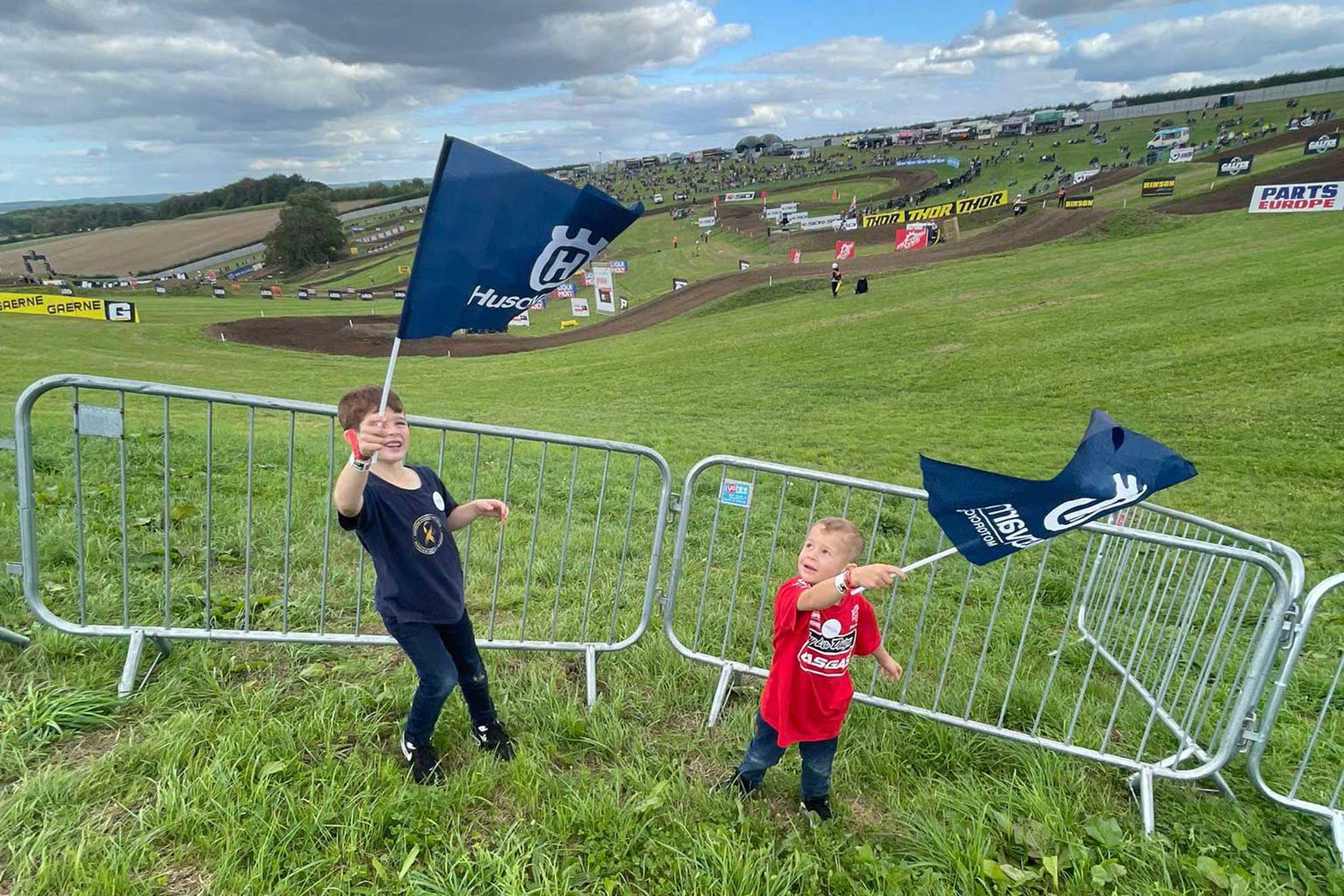 George and brother, Charlie waving flags with the British Motocross Championship course in the background.