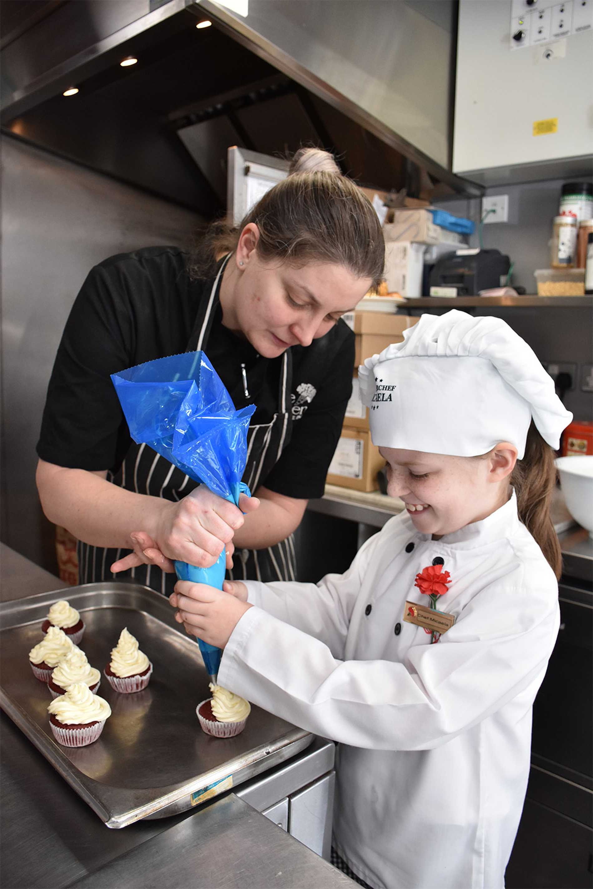 A member of the Reubens Hotel team helping Micaela to ice a tray of cupcakes.