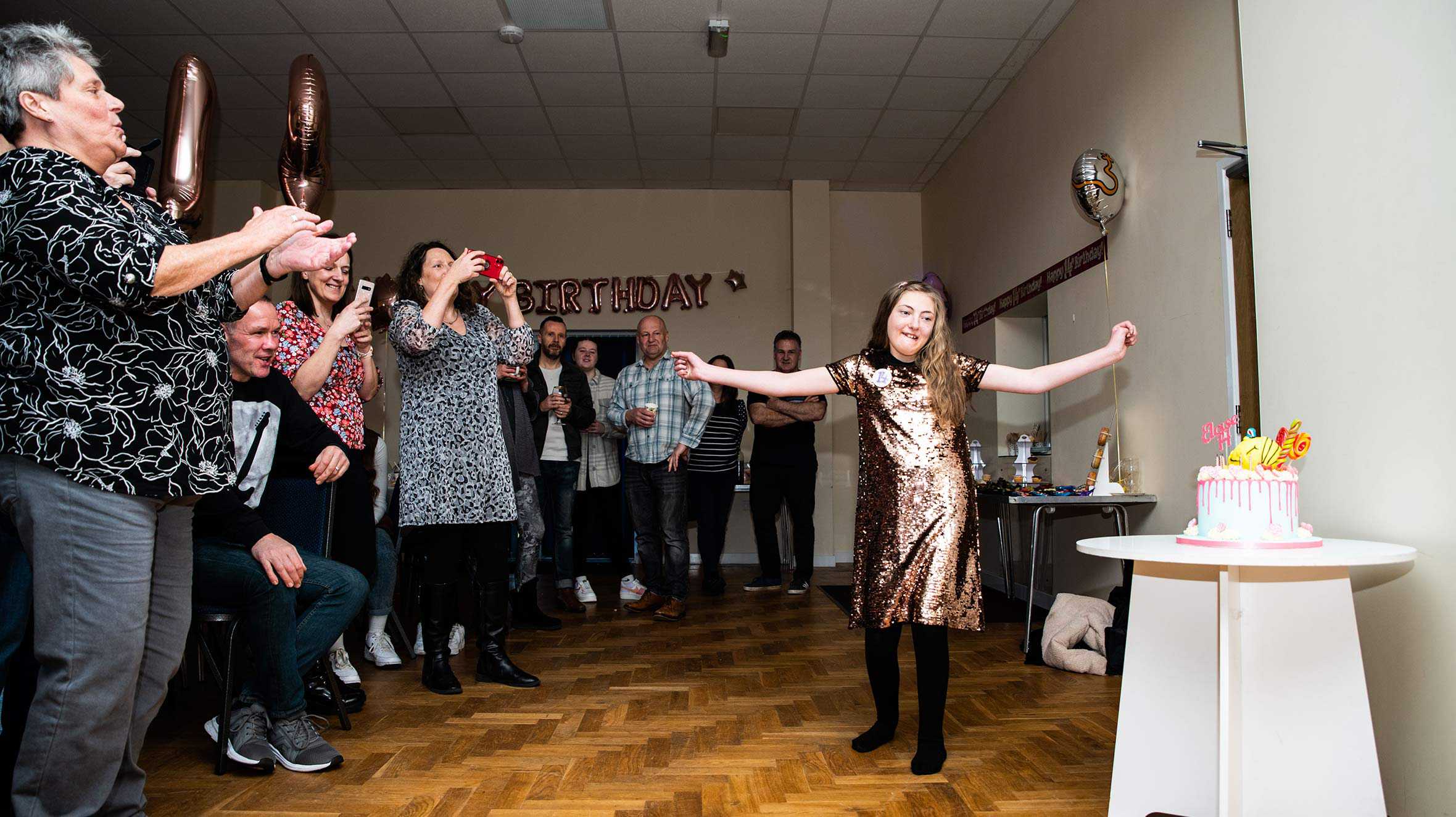 Eloise's guests applauding as she is presented with her birthday cake.