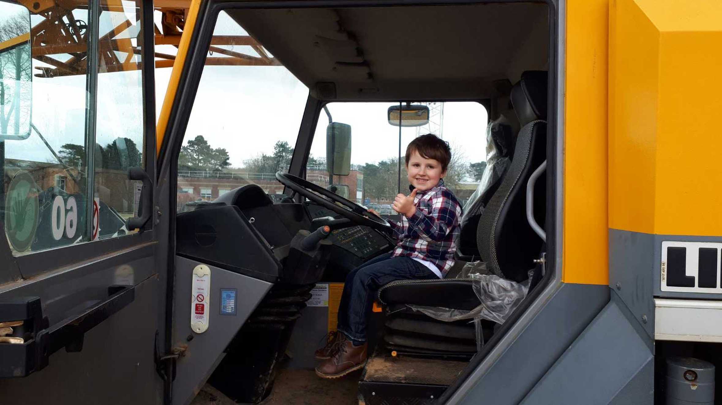 Joseph sitting in the driver's seat of a digger, giving a thumbs up.