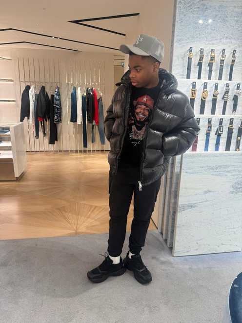 Rayondre stands in a shop with his hands in his pockets. Behind him is a railing of clothes
