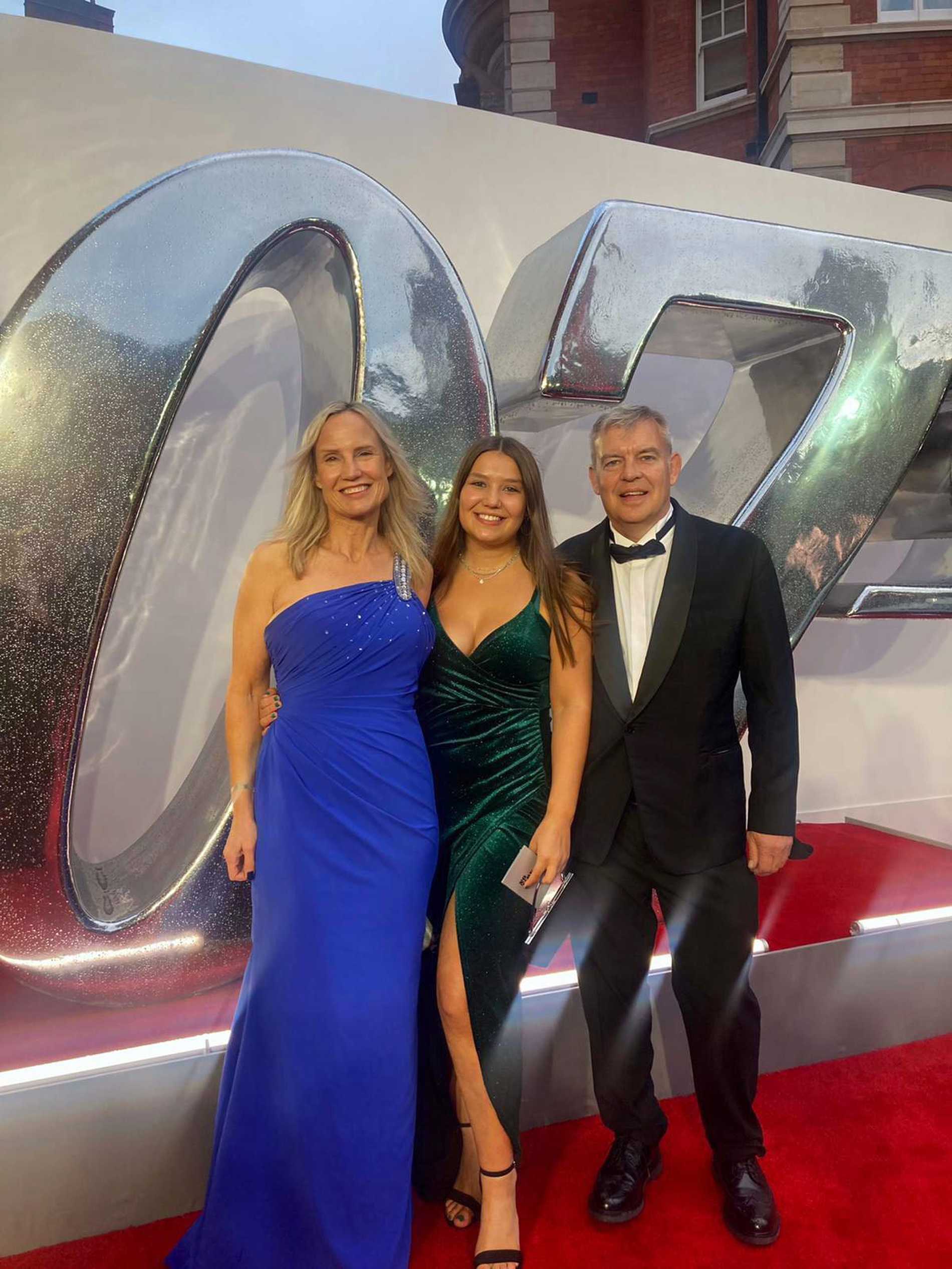 Chloe and her parents posing on the red carpet, in front of a large silver 007.