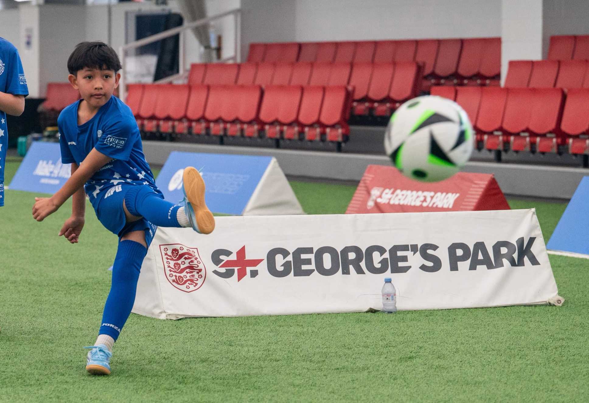 A shot of Liam just after he has kicked a football powerfully, with the ball in front of him