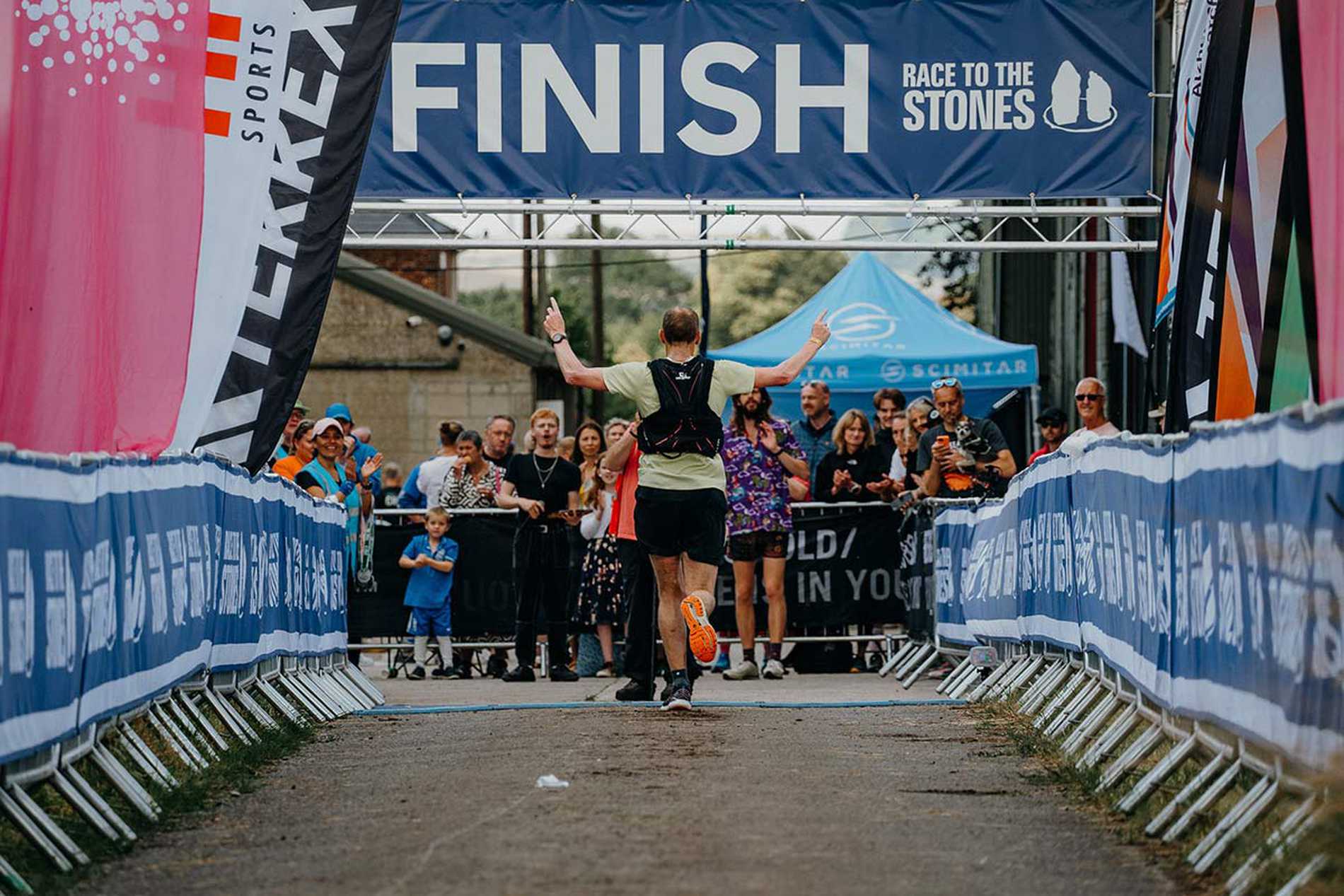 A runner raises their arms in the air as they cross the finish line to complete the Races to the Stones challenge.