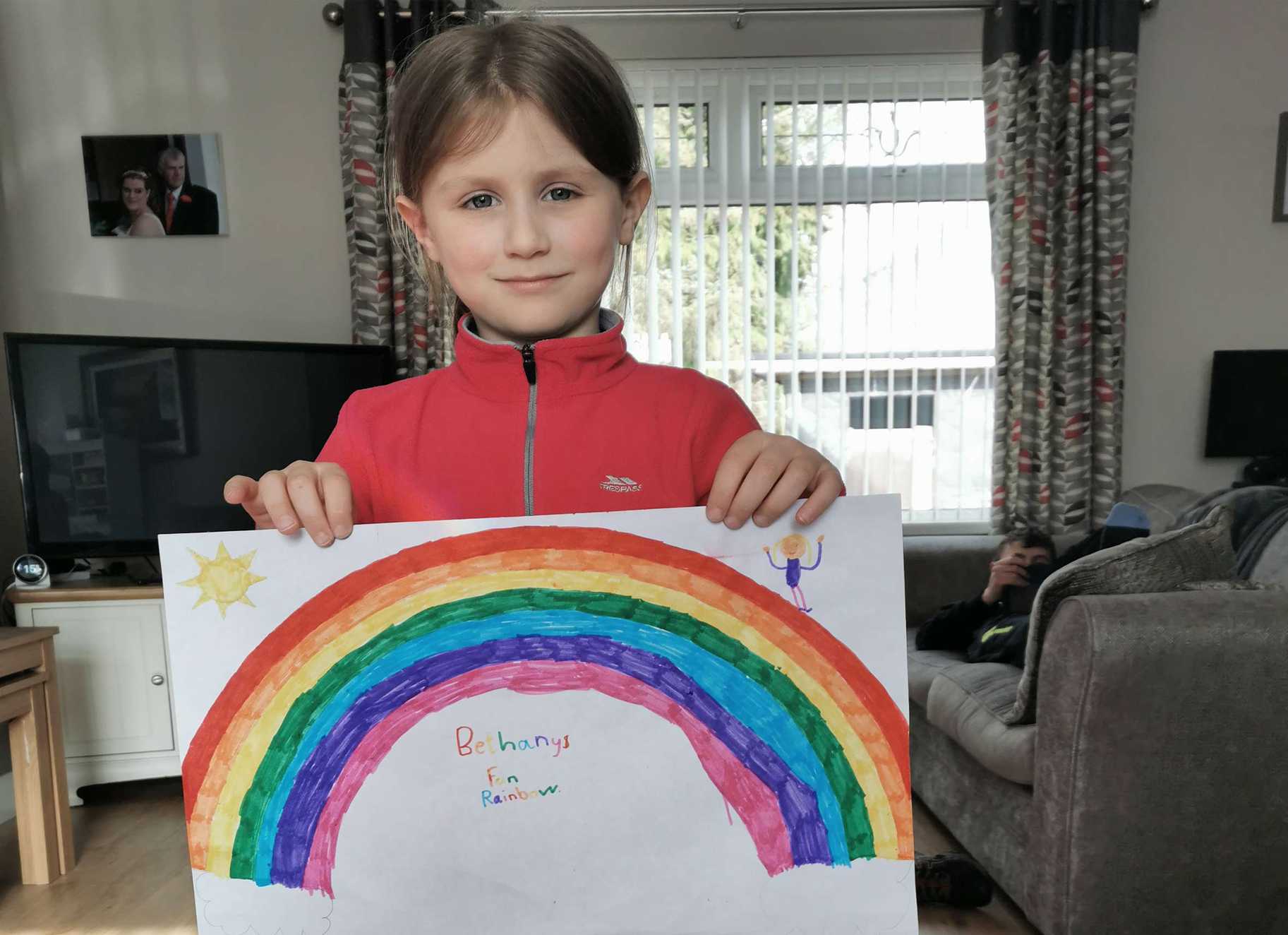 Bethany wearing holding a picture of a rainbow she painted.