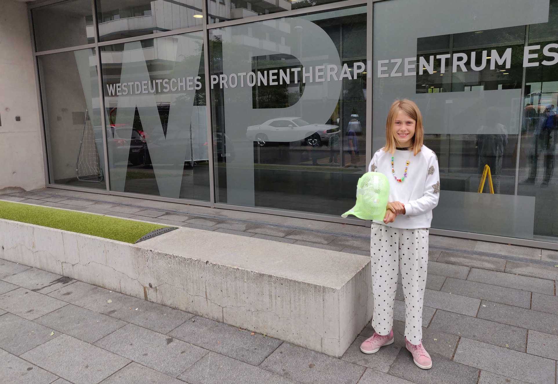 Leila smiling bravely as she holds the mask she had to wear for her proton treatment.