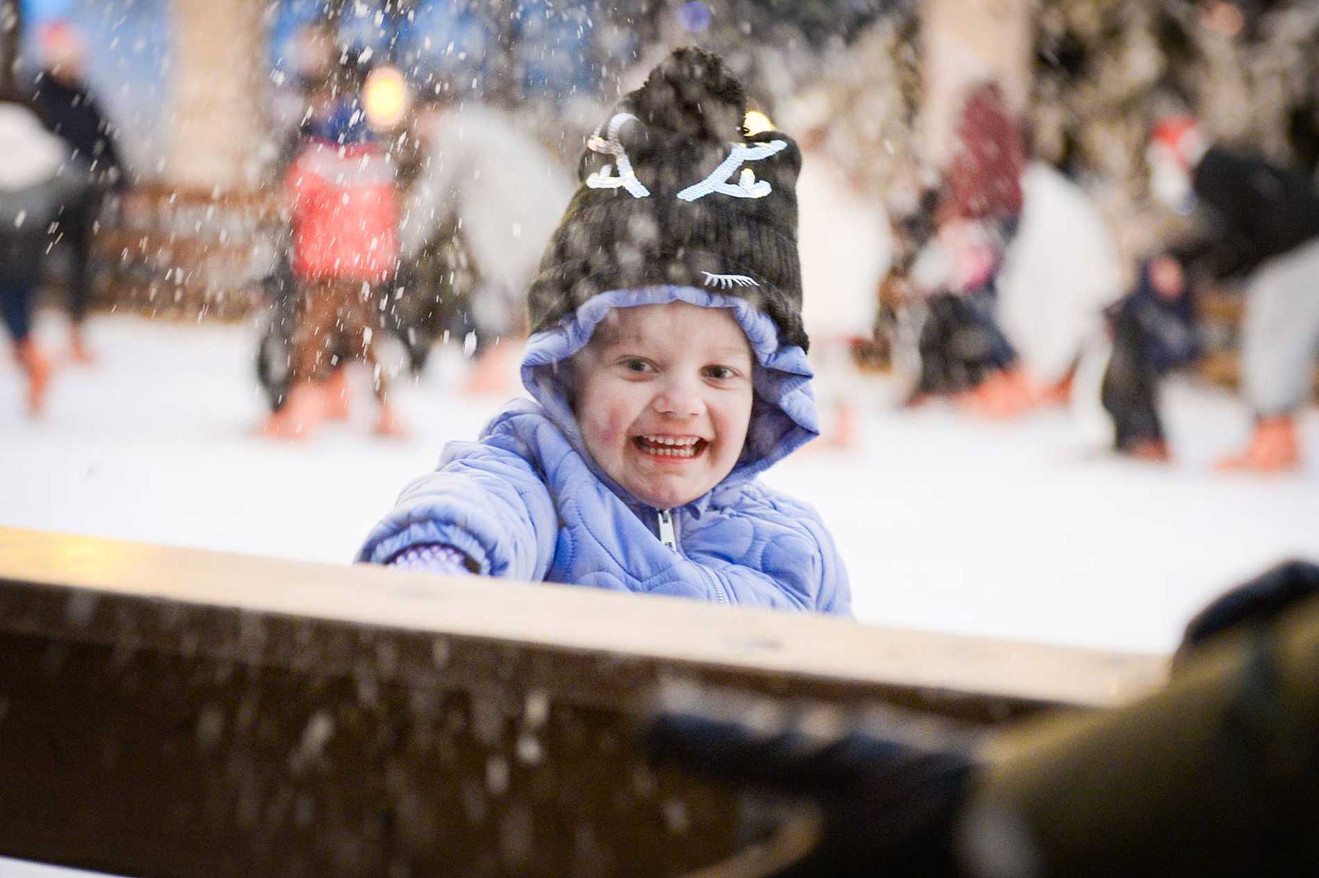 A close up of Julia standing by the edge of the ice rink throwing snow in the air with a huge smile on her face.