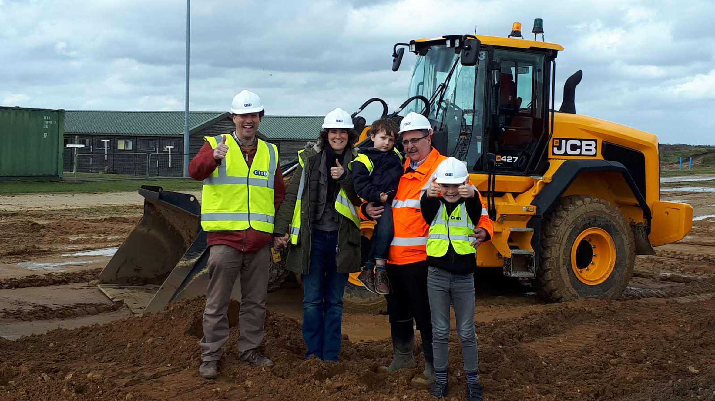 Joseph and his family standing in front of a digger at the construction site