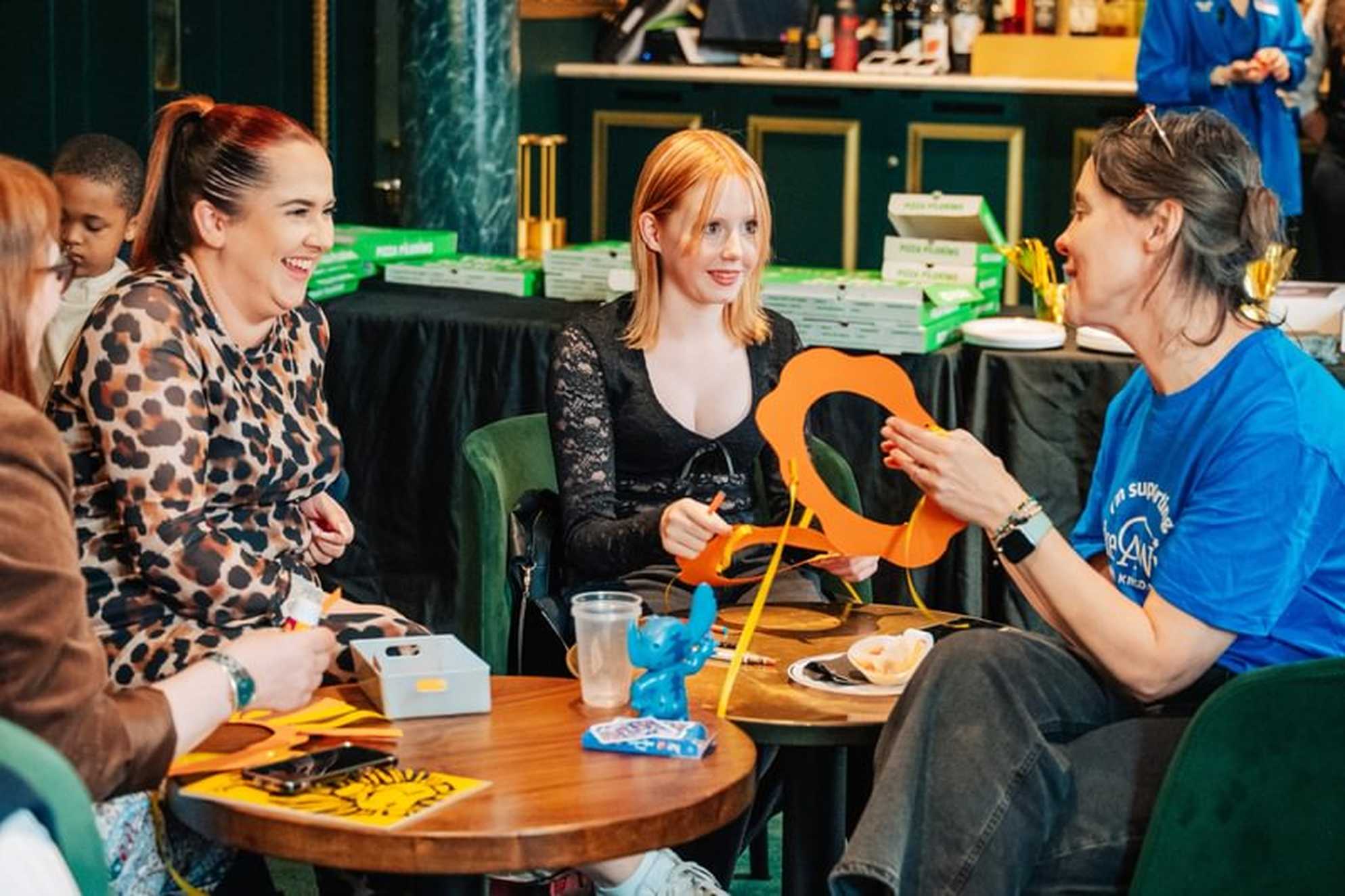 Faith and her mum sit around a table with volunteer Clare holding props from The Lion King