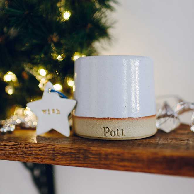 A Pott candle and porcelain star with a blue ribbon on a rustic wooden shelf.