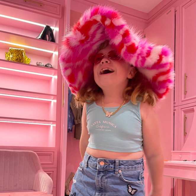 Sienna wearing a flamboyant pink fur hat in a matching pink room.